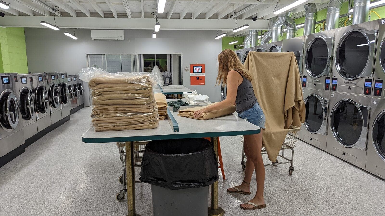 A customer folding a large blanket at one of the folding tables, with stacks of folded blankets beside her